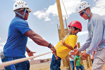 Jacob Thomas clings to a guide rope as he tries to traverse a tight wire aided by ropes course instructors Shawn Kelly, left, and Everette Denny during the Family Health and Wellness Conference at Piñon High School Tuesday. © 2011 Gallup Independent / Cable Hoover